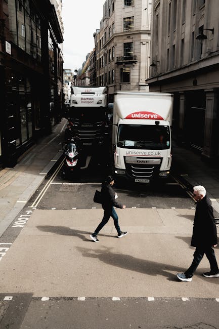 A person wearing a grey knitted sweater is seen guiding a medium-sized cardboard box wrapped with clear packing tape, with a red 'H' logo and moving labels, during a house removal process inside a res