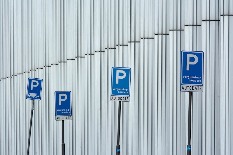 Four blue parking signs with a white 'P' symbol are mounted on black metal posts in front of a modern, vertically ribbed metallic building exterior. The signs display additional text including 'vergun